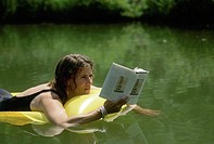 Woman, 30-40 years old, reading book while floating in water on an inflatable raft. Midwest, USA