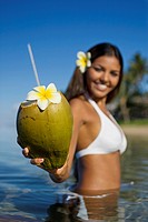Smiling, attractive local girl holds out a coconut with straw and flower ready to drink at Lahaina, Maui, Hawaii
