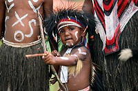 Half body image of cute, little young nacked Papuan boy with traditional body paint, looking at the camera and holding bow and arrow while aiming on t...