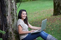 Teen girl sitting by tree using laptop