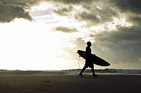 Silhouette of a surfer walking with his surfboard along the beach with stormy clouds in the background, Tarifa, Andalucia, Spain