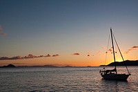 Silhouette of sailboat moored in water with orange glow of sunset lighting up the clouds and sky in Caribbean