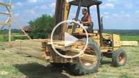 Forklift unloading lumber at construction site, external audio.