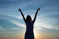 Silhouette of a young woman at dusk arms raised