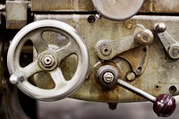 A metal wheel and lever on a piece of metalworking machinery.
