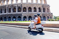 Couple riding a white vespa at the Roman Coliseum Rome Italy