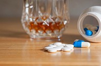 Close up of medical tablets and capsules with alcoholic drink in the background