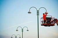 a workman working at height on a high access platform maintaining a street lamp light UK