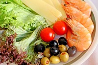Salad plate of cheese, olives, tomatoes, shrimp and lettuce on white plate with green trim  White tablecloth  Green and black olives  Full frame
