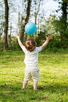 child throwing ball in midair, arms stretched out and up, from back
