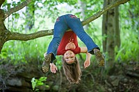 Young girl hanging upside down on branch of tree