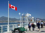 People walking on the deck beside Canada Place, with Canadian flags in the background