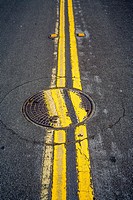 A carelessly replaced manhole cover interrupts two parallel lines on a street in San Clemente, CA