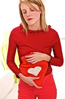 Young blond woman holding a red heart shaped hot water bottle