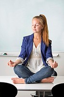 Attractive businesswoman sitting barefoot in yoga position on a table in her workplace