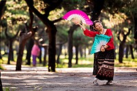 An elderly Chinese woman practices tai chi fan dance martial arts exercise early morning at the Temple of Heaven Park during summer in Beijing, China