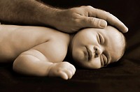 A newborn baby isolated on black sleeps while the father strokes the head