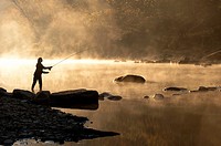 Silhouette profile of a young woman casting with a fly fishing rod by a stream early in the morning, north central, Alabama, USA.