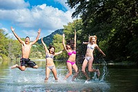 Group of teenagers having summer fun while jumping out of the water