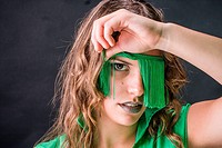 Young woman looking out from a blindfold of green fringes