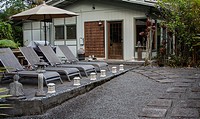 exterior view of a Japanese inspired house with stone deck, stepping stones, Buddha statue, stone lanterns and lounge chairs.