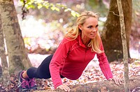 A 38 year old blond woman wearing work-out clothing doing a push-up on a log in a forest setting in the fall