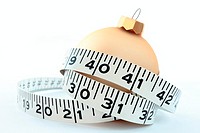 a christmas eating & excess concept featuring a tape measure around a gold coloured bauble