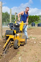 Young Caucasian man of 24 years is operating a walk-behind trencher to make a ditch for pipes and cable