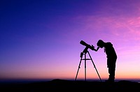 The silhouette of a teenage boy stargazing with a telescope at dusk