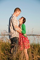 Standing in tall grass is a mixed race couple arm in arm.