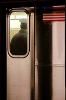 Back of an NYPD police officer seen through the window on an MTA subway car, with the car's US flag sticker next to him.