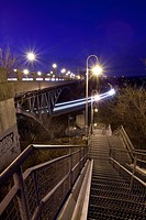 A steel stairwell leading down under a bridge with a train passing by in Hamilton, Ontario, Canada.