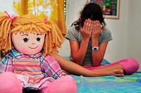 A young girl hides her face and cries on her bed in her bedroom.