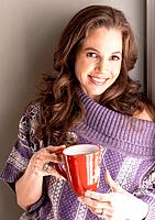 37 year old brunette woman wearing a big sweater and holding a cup of steaming tea in a kitchen setting.