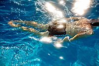 A man underwater swimming as sunlight reflects off the bright blue water.