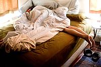 A woman sleeping sideways on a bed in the afternoon with her legs dangling off the side.
