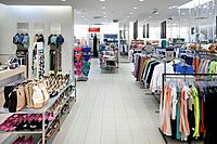 Fashion shop interior with display. Clothing and bags in retail store. Large aisle and elevated view.