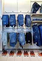 Jeans, trousers and shoes in retail shop interior. Store display with rack, shelf.