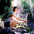 A girl with a backpack and hiking shoes holding her hands out under a waterfall off the Multnomah-Wahkeena Loop Trail in Oregon.