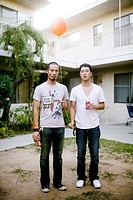 Two Asian men holding beers and a balloon in a courtyard in an apartment complex in Los Angeles