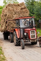 Tractor with large loads of baled hay on a village road.