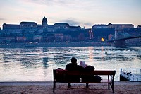 A couple rest in the shore of the Danube river, in front of the Royal Palace.