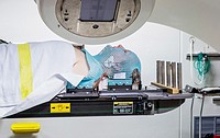 Male cancer patient lying under a linear accelerator or linac receiving radiation treatment. Radiotherapy is the use of high-energy x-rays (and other ...