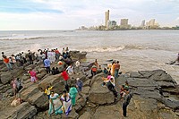 indian people enjoy fresh breeze from arabian sea on a rocky area outside the haji ali´s mosque and tomb in worli district. mumbay. maharashtra. india...