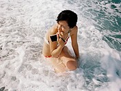 A young woman with her camera sits in foamy water on the beaches of Chi Shing Tan in Hualien, Taiwan