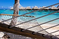 Rope hammock on a beach with overwater bungalows by the turquoise waters of Moorea in French Polynesia.
