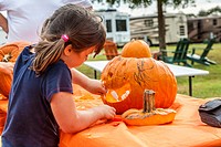 Young girl inserts teeth while decorating a pumpkin for Halloween in an RV resort park in Florida.