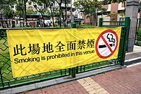Hong Kong, China, Asia. Hong Kong Kowloon. Large yellow bilingual banner in english and chinese at the entrance to a small urban park advising that ""...