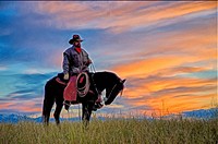 Cowboy on horseback against vibrant dawn sky.