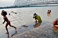 Indian people bathing in Hooghly River next to Howrah Bridge, Kolkata, India.